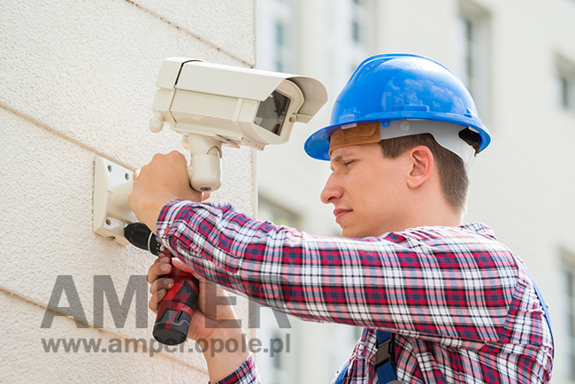 technik montuje kamerę monitoringu na ścianie budynku